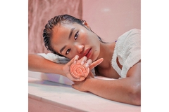 An Asian woman with wet hair holds up a circular bar of soap.